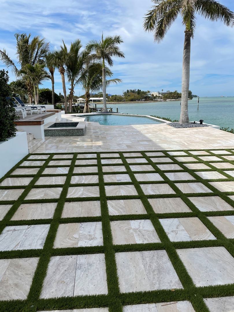 Paver-and-grass grid patio leading to a waterfront deck lined with palms